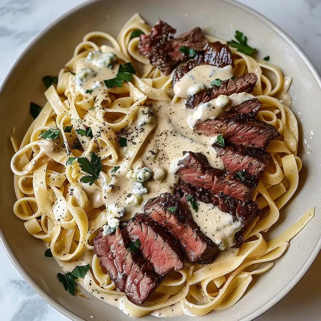 Un plat de tagliatelles accompagné de tranches de bœuf et sauce onctueuse, décoré de persil et fromage bleu.