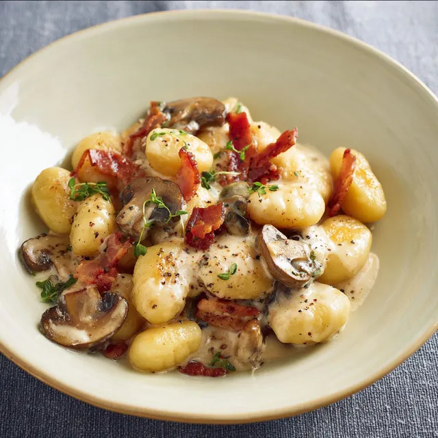 Gnocchis au fromage crémeux accompagnés de champignons et de bacon croustillant.