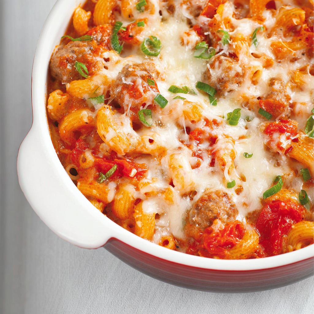 Un plat de macaronis garnis de tomates et de saucisses italiennes dans une casserole en verre.