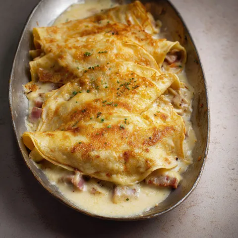 Une délicieuse crêpe garnie de jambon et béchamel gratinée est présentée sur un plat argenté.