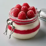 Un dessert en verre avec couches de framboises et crème mascarpone.