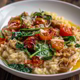 Plat de risotto au veau, aux tomates et aux épinards, servi sur bois.