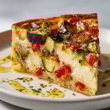 Une tranche de flan salé avec légumes méditerranéens et fromage gratiné, présentée sur une assiette.