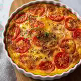 Une quiche moelleuse sans pâte, préparée avec du thon et des tomates fraîches, présentée dans un plat en verre.
