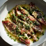 Filets croustillants de rougets dorés servis avec persil et ail sur une assiette.