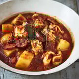 Un bol blanc rempli de calamars et chorizo en sauce.