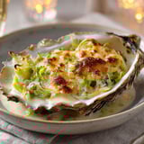 Des huîtres gratinées aux poireaux dans une belle assiette, accompagnées de vin.