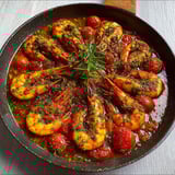 Poêle remplie de gambas dorées à l'ail, tomates et herbes fraîches.