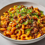 Des macaronis au bœuf assaisonné et au gochujang avec des herbes vertes et des graines de sésame bien grillées.