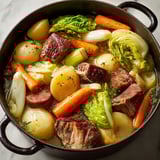Un généreux pot-au-feu aux multiples viandes et légumes anciens servi dans un grand plat.