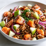 Un plat frais de lentilles avec des morceaux de saumon, des noix et de la pomme.